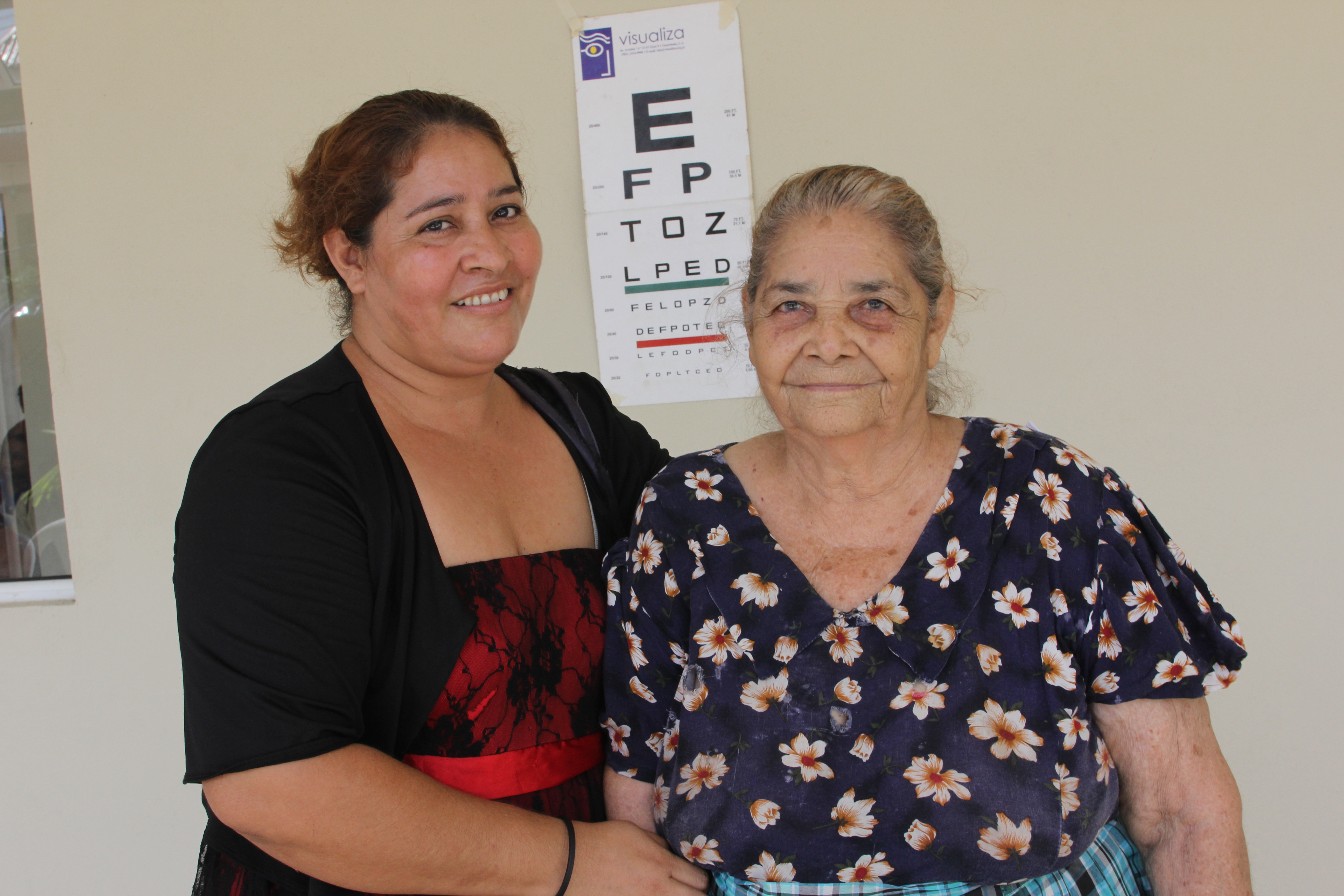 Two women stand in front of an eye chart