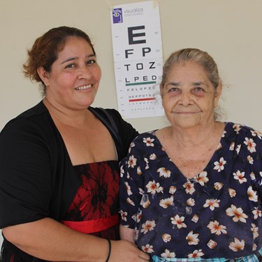 Two women stand in front of an eye chart